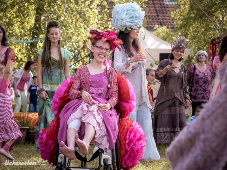 Sonniges Festival mit tanzenden Menschen und fröhlichem Mädchen im Rollstuhl, geschmückt mit bunten Blumen.