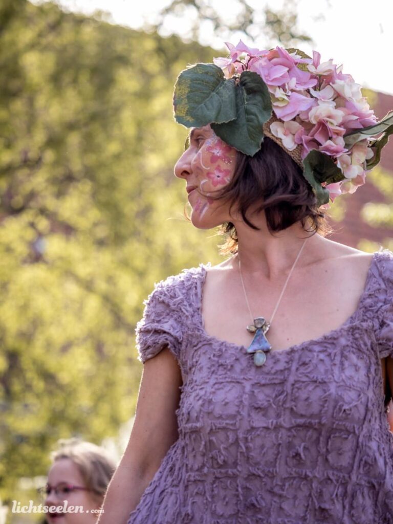Eine Frau mit Blumenkranz und Bodypainting in einem festlichen Ambiente, umgeben von grüner Natur.