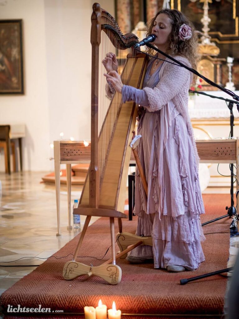 Eine Musikerin spielt Harfe und singt in einer Kirche, umgeben von Kerzenlicht und festlicher Atmosphäre.
