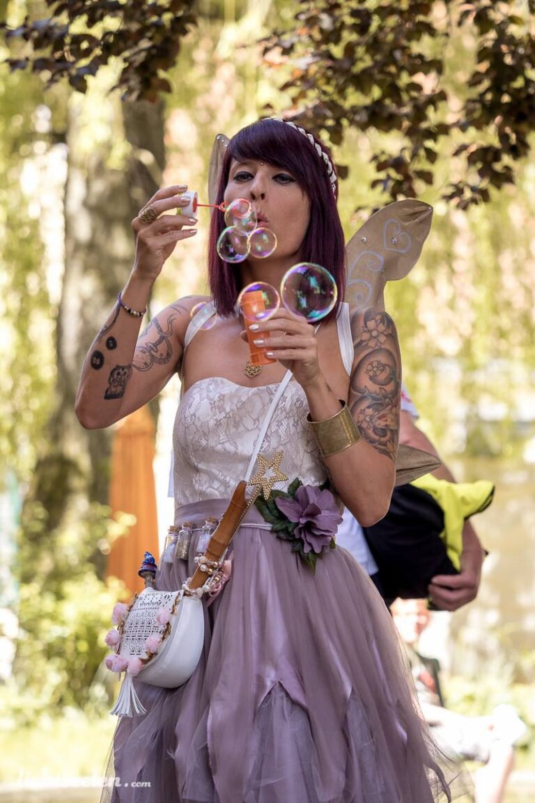 Junge Frau mit Flügeln bläst Seifenblasen in einem festlichen Umfeld, gekleidet im Boho-Stil.