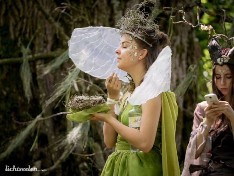 Eine mystische Frau in einem grünen Kleid mit Flügeln und Naturdekorationen, die an einem Wald-Festival teilnimmt.