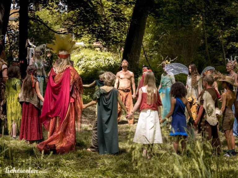 Eine Gruppe von Menschen in fantasievollen Kostümen feiert gemeinsam in einer sonnigen Waldlichtung.