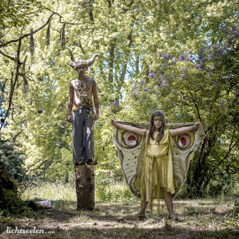 Zwei fantasievoll verkleidete Personen in einem sonnigen, grünen Wald, die magische Stimmung ausstrahlen.