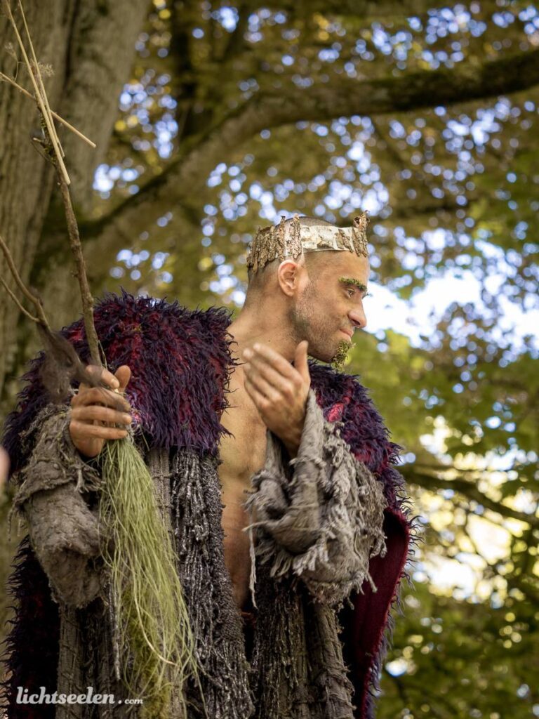 Ein faszinierender Mann in einem kunstvollen Gewand mit Krone, der inmitten der Natur applaudiert.