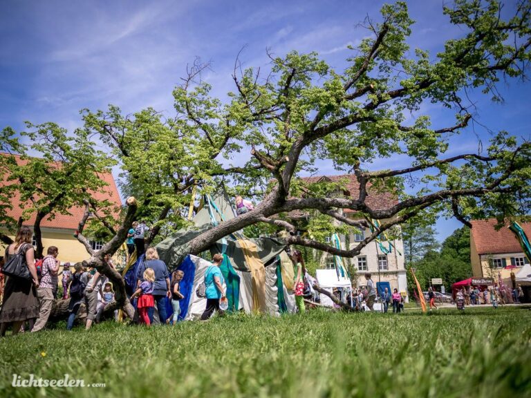 Festliche Menschenmenge unter einem blühenden Baum bei einem Event in einer malerischen bayerischen Umgebung.