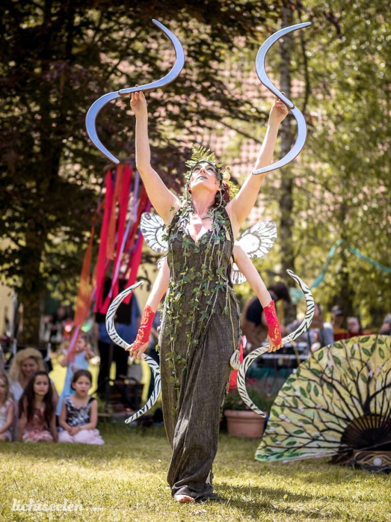 Eine Tänzerin in fantasievoller Kostümierung führt eine anmutige Darbietung im Freien während eines Festivals auf.
