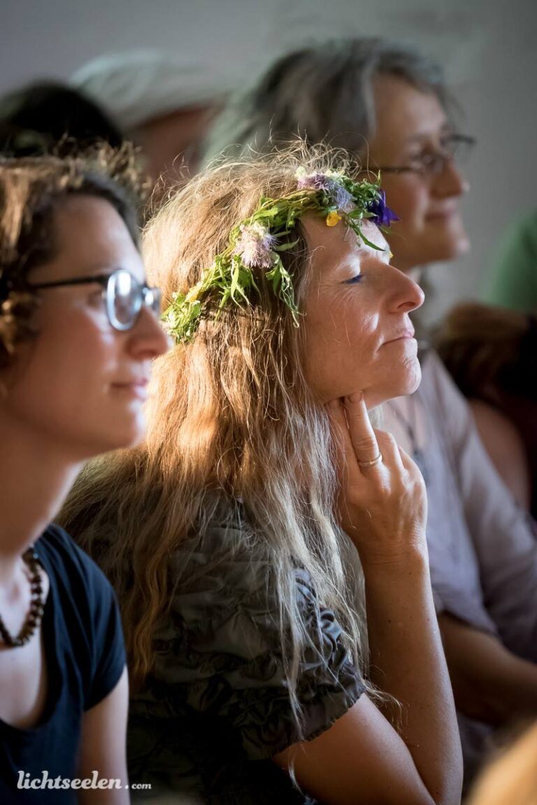 Eine entspannte Frau mit Blumenkranz sitzt bei einer Veranstaltung und genießt den Moment.
