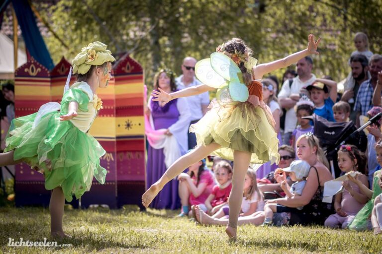 Zwei tanzende Feen in bunten Kostümen verzaubern das Publikum auf einem Festival im Freien.
