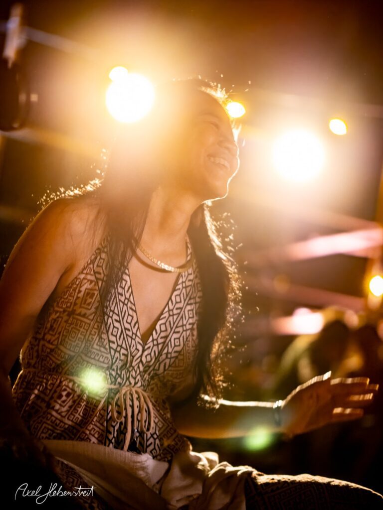 Strahlendes Lächeln einer Frau auf einem Konzert, umgeben von warmem Licht und festlicher Atmosphäre – © Axel Hebenstreit