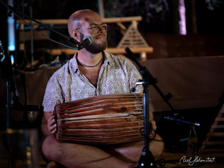Ein lächelnder Musiker spielt ein traditionelles Instrument auf einem Festival im Freien – © Axel Hebenstreit.