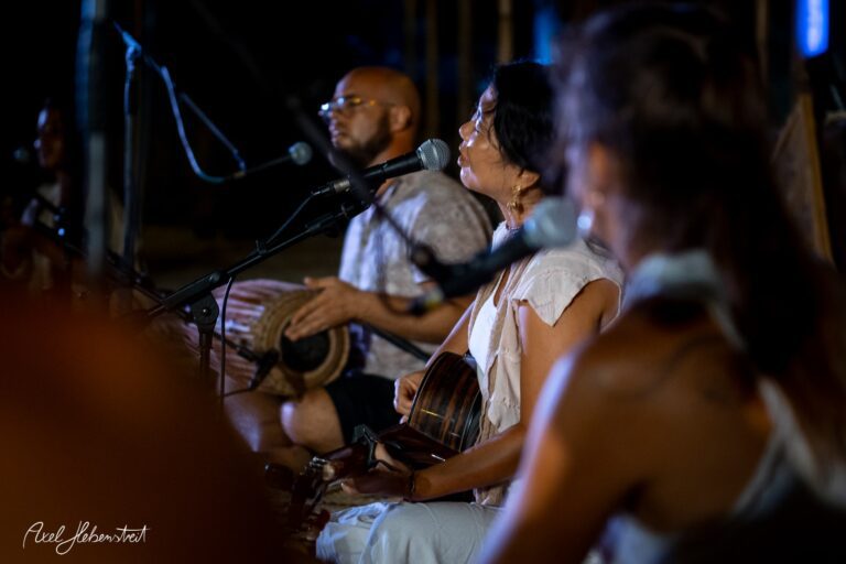 Musikerin singt leidenschaftlich in eine Mikrofon, während ein Percussionist im Hintergrund spielt – © Axel Hebenstreit