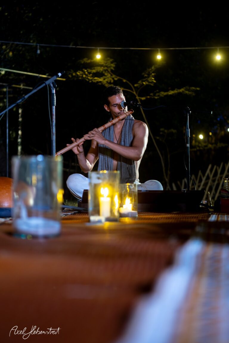 Ein Musiker spielt in entspannter Atmosphäre Flöte, umgeben von Kerzenlicht und Natur – © Axel Hebenstreit