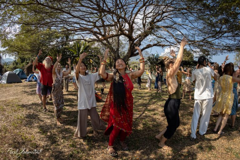 Eine Gruppe fröhlicher Menschen tanzt unter Bäumen bei einem Festival in der Natur. – © Axel Hebenstreit