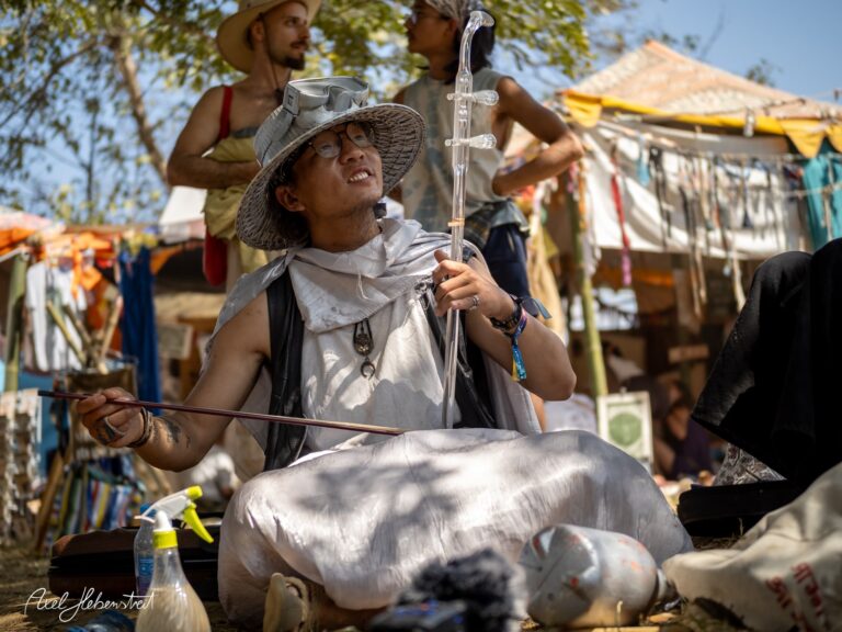 Ein junger Mann spielt konzentriert auf einem traditionellen Instrument in einer lebhaften Festivalatmosphäre – © Axel Hebenstreit