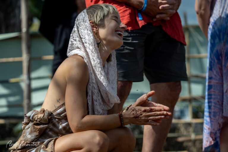 Lachende Frau mit Henna, die im Kreis sitzt und Freude bei einem Festival teilt – © Axel Hebenstreit