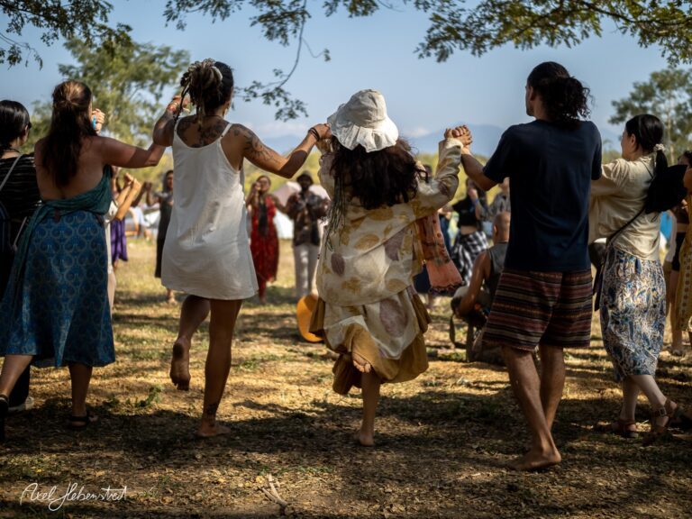 Tanzende Menschen in einer fröhlichen Kreisformation unter Bäumen während eines Festivals – © Axel Hebenstreit