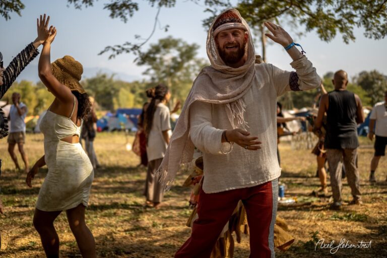 Menschen tanzen fröhlich auf einem Festival im Freien, umgeben von Natur und festlicher Stimmung – © Axel Hebenstreit.