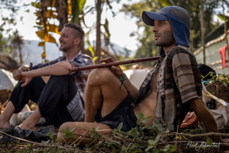 Zwei Männer sitzen entspannt in der Natur, einer spielt auf seiner Flöte, die Stimmung ist harmonisch und friedlich. – © Axel Hebenstreit