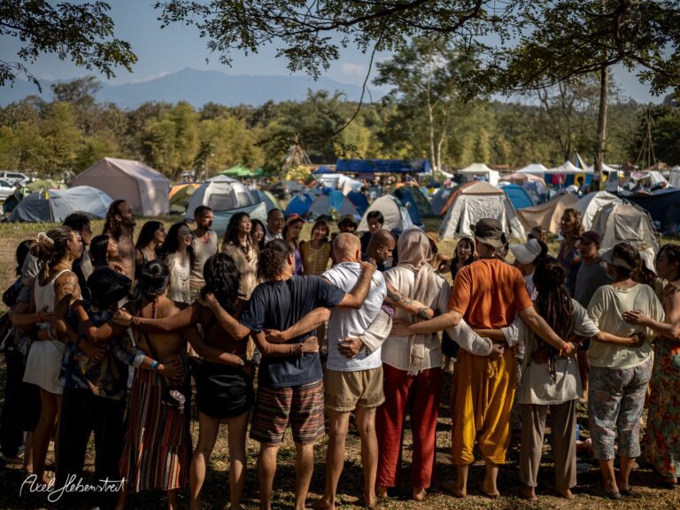 Eine vielfältige Gruppe von Menschen umarmt sich in einem harmonischen Kreis auf einem Festivalgelände – © Axel Hebenstreit