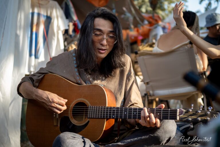 Junger Mann spielt entspannt Gitarre in einer festlichen Umgebung unter freiem Himmel – © Axel Hebenstreit