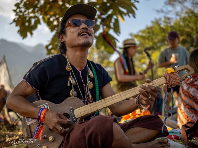 Ein Musiker spielt fröhlich auf einer Gitarre im Freien während eines Festivals in der Natur – © Axel Hebenstreit.