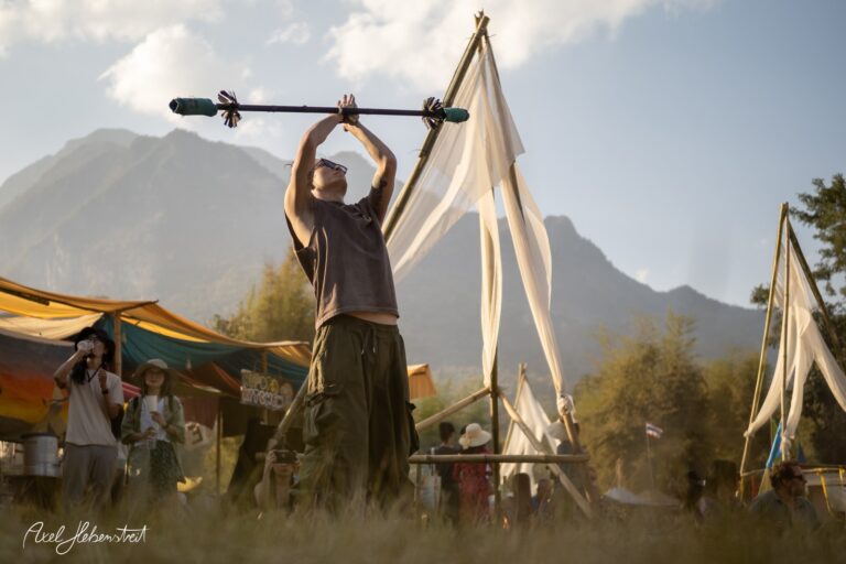 Ein Akrobat hebt einen langen Stock im Sonnenlicht während eines Festivals in den Bergen – © Axel Hebenstreit