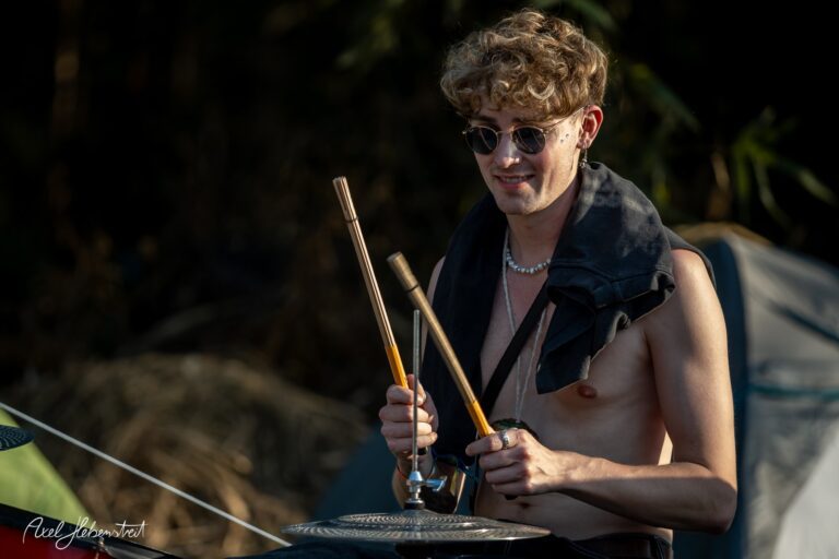 Junger Mann spielt mit Holzstöcken auf einem Instrument in einer entspannten Festivalatmosphäre – © Axel Hebenstreit.