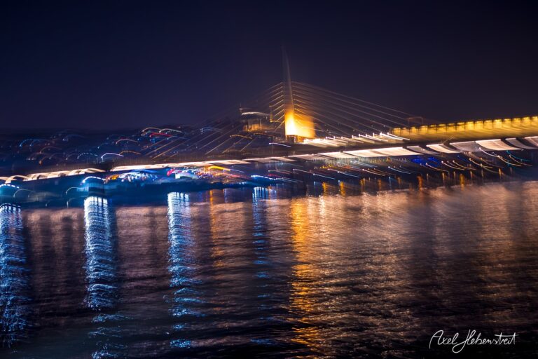 Faszination einer beleuchteten Brücke über dem Wasser bei Nacht mit bunten Lichtreflexionen – © Axel Hebenstreit