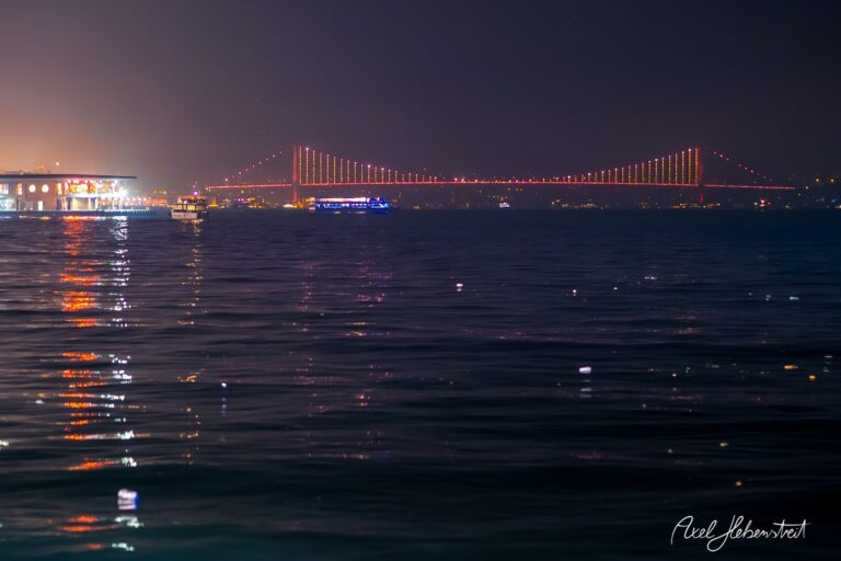 Lichter einer Brücke spiegeln sich im ruhigen Wasser bei Nacht, Atmosphäre von Frieden und Schönheit – © Axel Hebenstreit