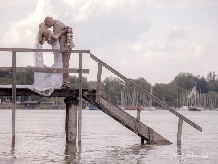 Braut und Bräutigam in romantischer Umarmung auf einem Steg über dem Wasser – © Axel Hebenstreit
