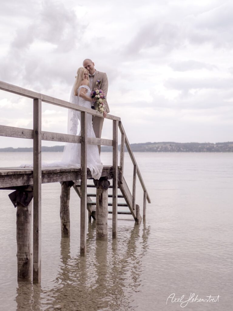 Brautpaar auf einem Holzsteg am Wasser, umgeben von einer romantischen Stimmung – © Axel Hebenstreit