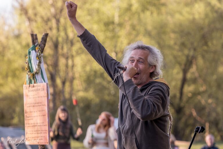 Ein leidenschaftlicher Sänger mit erhobener Faust auf einer Bühne umgeben von Natur – © Axel Hebenstreit
