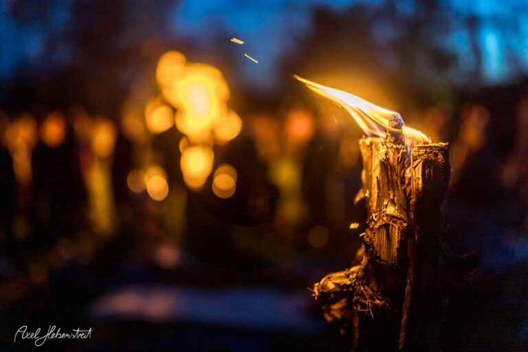 Fackel mit einer lebhaften Flamme vor unscharfem, festlichem Hintergrund – © Axel Hebenstreit