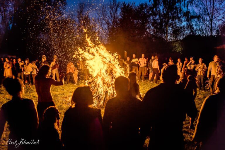 Tanzende Menschen um ein großes Feuer in einer nächtlichen Freiluftatmosphäre – © Axel Hebenstreit