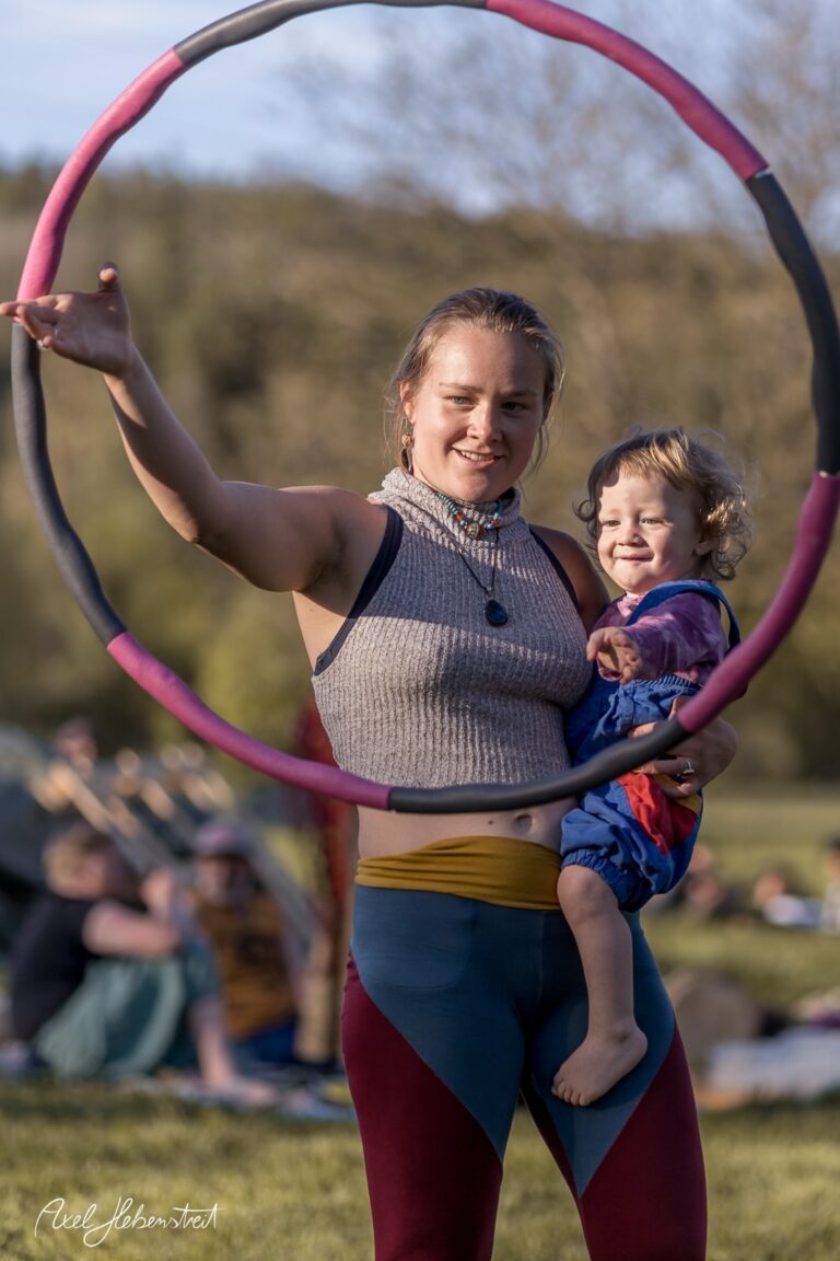 Frau mit Hulahoop-Reifen und lächelndem Kind auf einer Wiese, fröhliche Festivalstimmung – © Axel Hebenstreit
