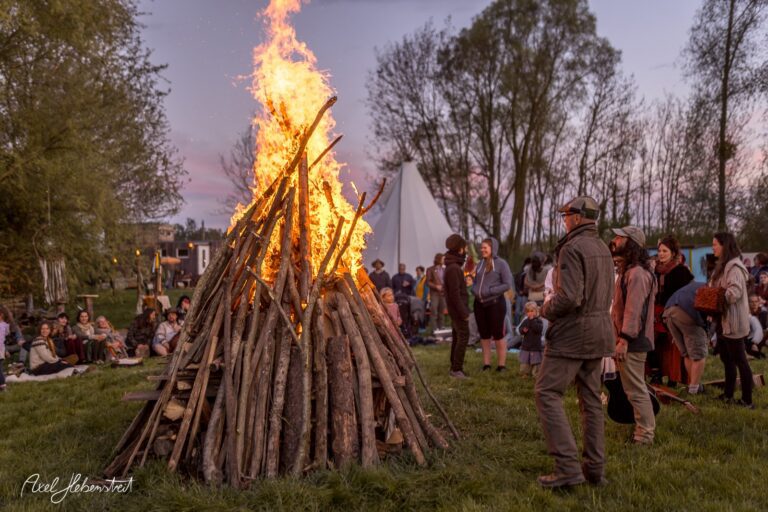 Flames rise from a large bonfire, while people gather around in a festive atmosphere im Freien. – © Axel Hebenstreit