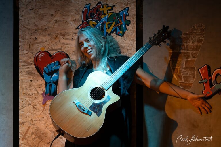 Eine Sängerin mit Gitarre in einem kreativen, urbanen Ambiente, voller Energie und Leidenschaft – © Axel Hebenstreit