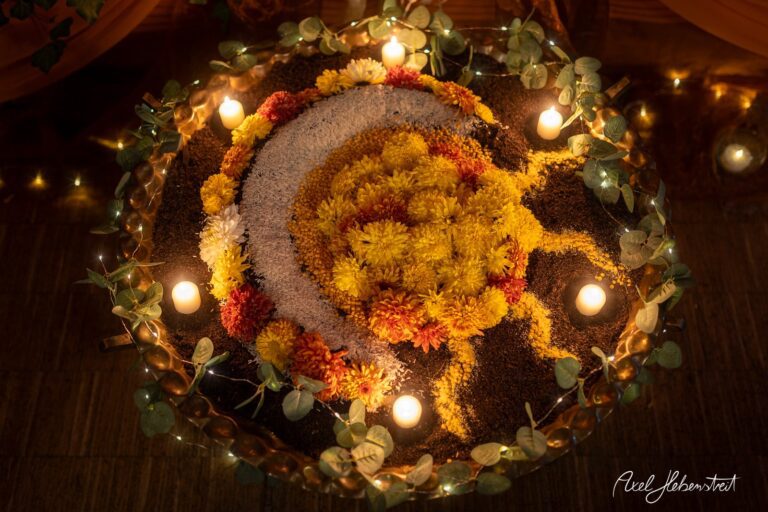 Bunte Blüten und Kerzen bilden ein kreatives Rangoli-Muster auf einem Tisch, festliche Stimmung verbreitend – © Axel Hebenstreit
