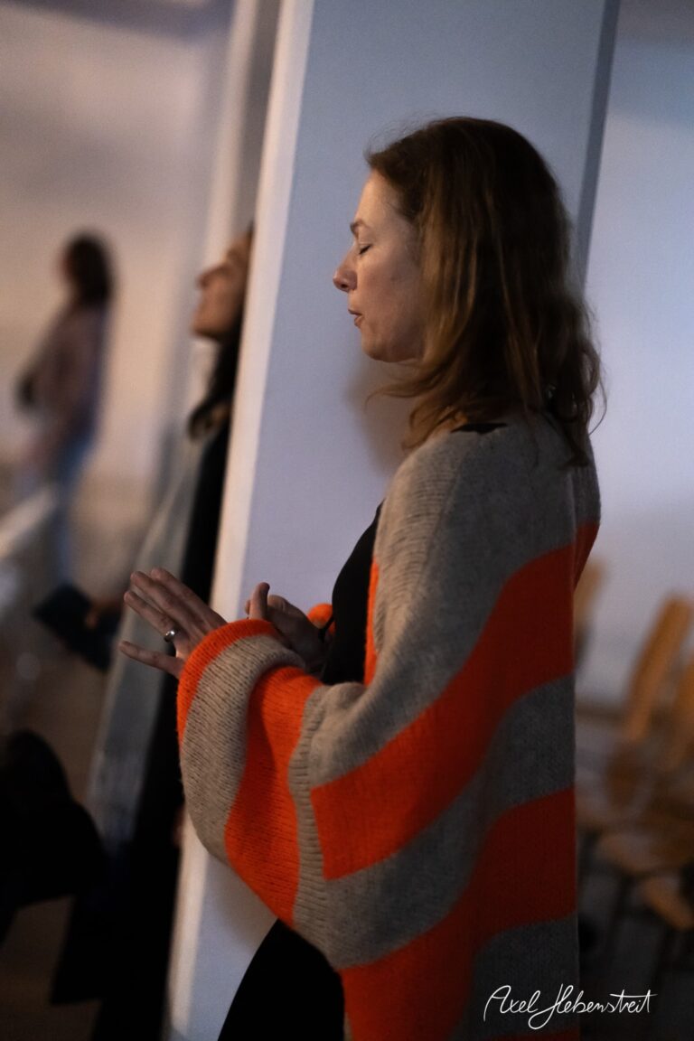 Frau mit gestreifter Strickjacke, nachdenklich und in einem entspannten Moment, in einem lichtdurchfluteten Raum – © Axel Hebenstreit