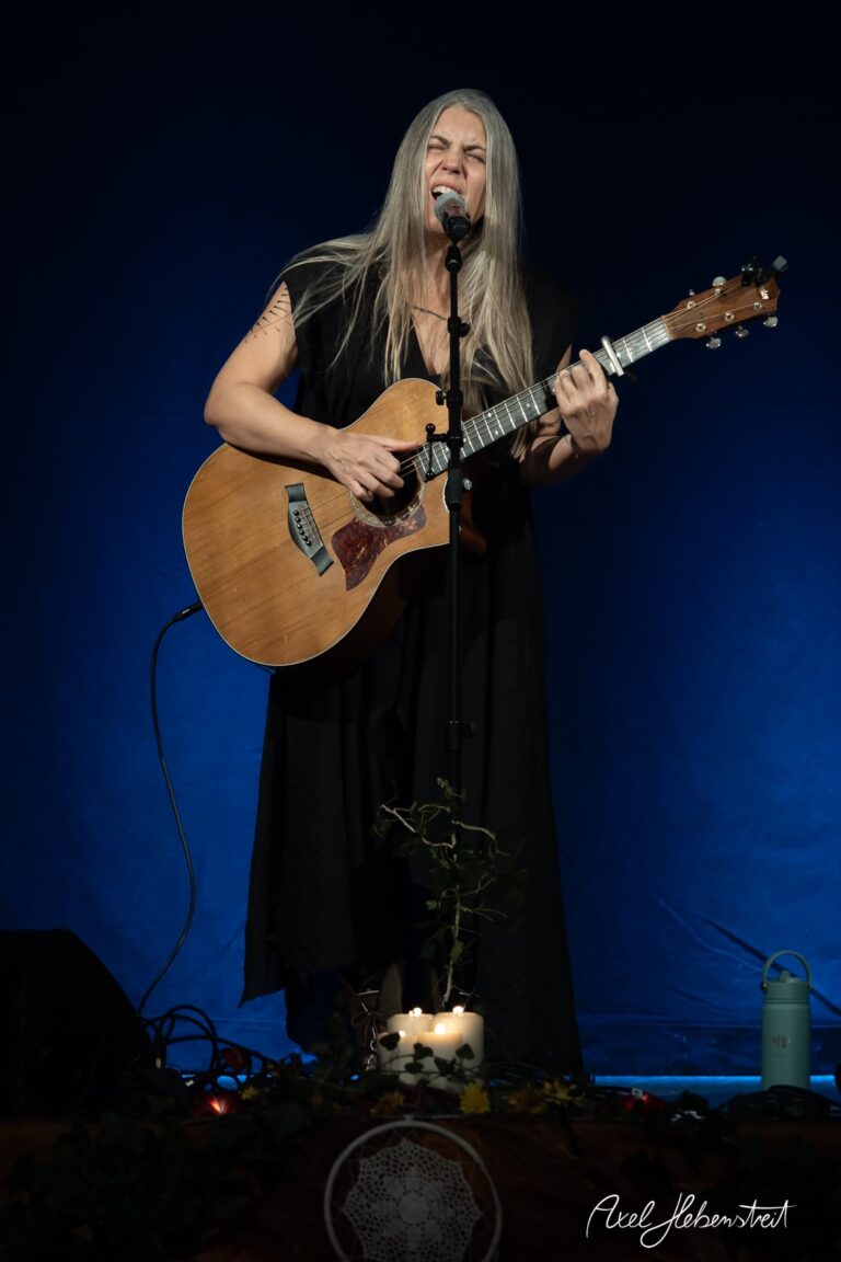 Frau in schwarzem Kleid spielt Gitarre und singt leidenschaftlich auf einer Bühne – © Axel Hebenstreit