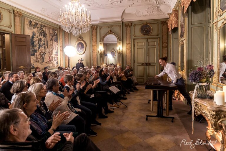 Ein Musiker spielt vor begeistertem Publikum in einem eleganten Saal, umgeben von opulenter Einrichtung. – © Axel Hebenstreit