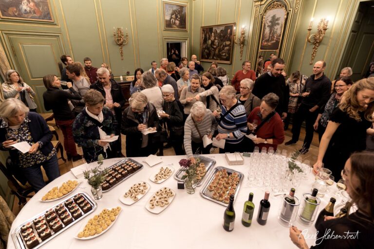 Ein festliches Buffet mit zahlreichen Gästen, die sich an köstlichen Häppchen und Getränken bedienen – © Axel Hebenstreit