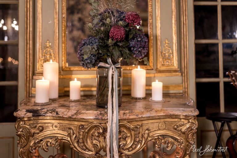 Eleganter Tisch mit einer Blumenvase und weißen Kerzen, die eine gemütliche Atmosphäre schaffen – © Axel Hebenstreit