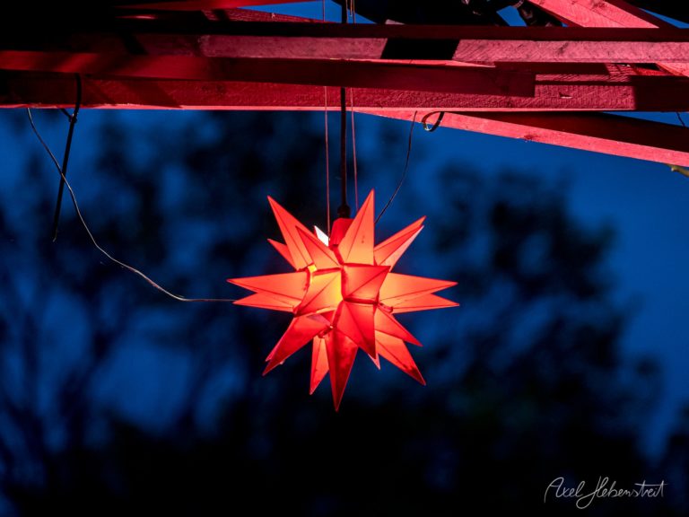 Leuchtender roter Weihnachtsstern gegen tiefblauen Himmel mit roten Holzbalken, festliche Dezemberatmosphäre – © Axel Hebenstreit