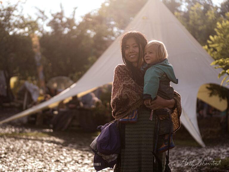 Eine Mutter hält ihr Kind beim Camping in der goldenen Stunde vor einem Zelt in der Natur – © Axel Hebenstreit