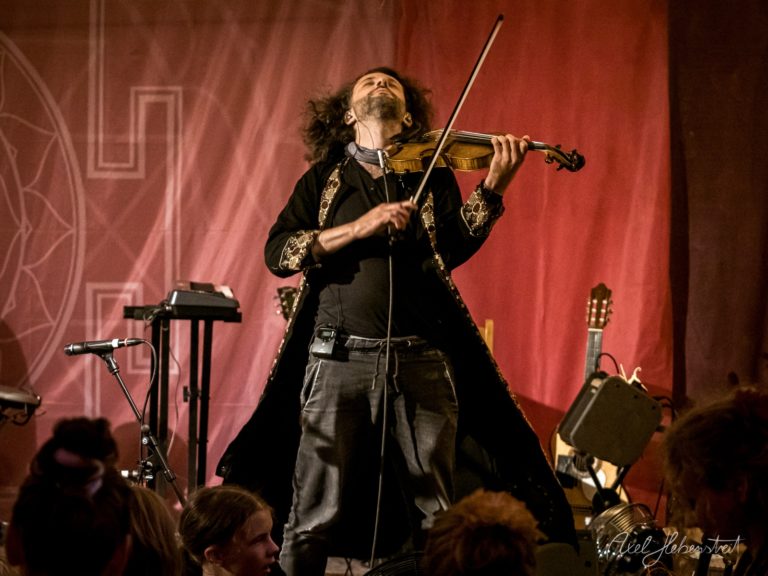 Violinist in schwarzem Anzug mit verzierter Weste spielt leidenschaftlich auf roter Bühne vor Publikum – © Axel Hebenstreit
