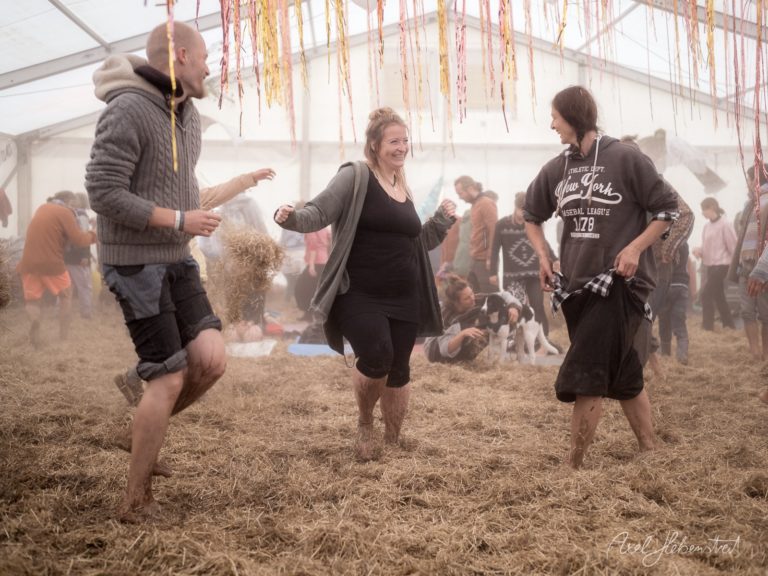 Fröhliche Menschen tanzen und springen in einem Festzelt auf Stroh bei einem bayerischen Festival – © Axel Hebenstreit