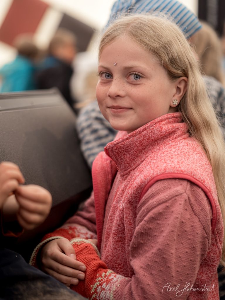 Junges Mädchen in rosafarbenem Pullover blickt über die Schulter in festlicher Atmosphäre – © Axel Hebenstreit