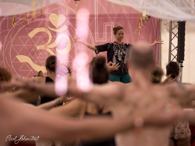 Yoga-Übung in einem Festivalzelt mit Fokus auf die anleitende Lehrerin und einer Gruppe von Teilnehmenden – © Axel Hebenstreit