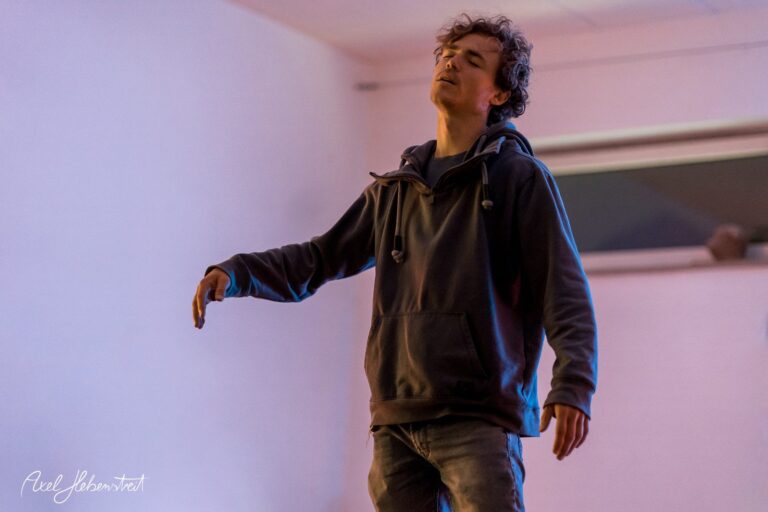 Ein junger Mann in einem Hoodie steht entspannt mit geschlossenen Augen in einem romantisch beleuchteten Raum – © Axel Hebenstreit
